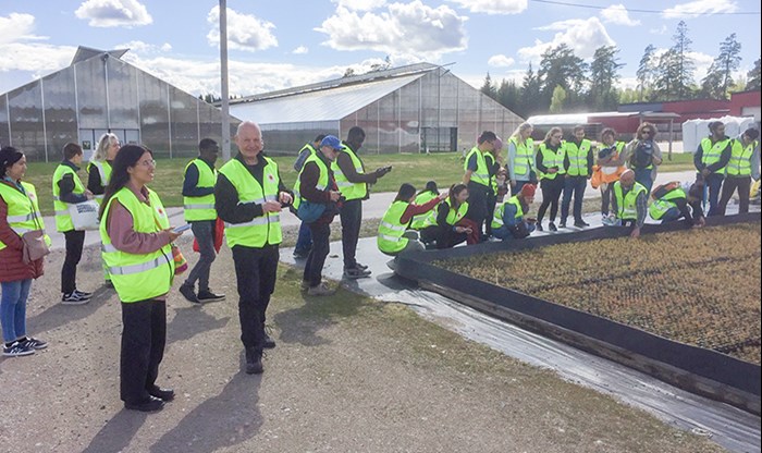 Ungefär 20 personer står utanför ett växthus där små plantor växer. Foto.
