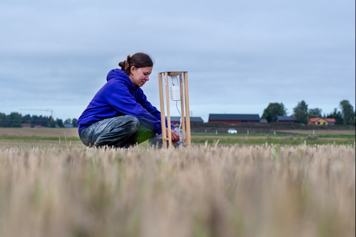 A woman by a camera mounted over a field. Photo.