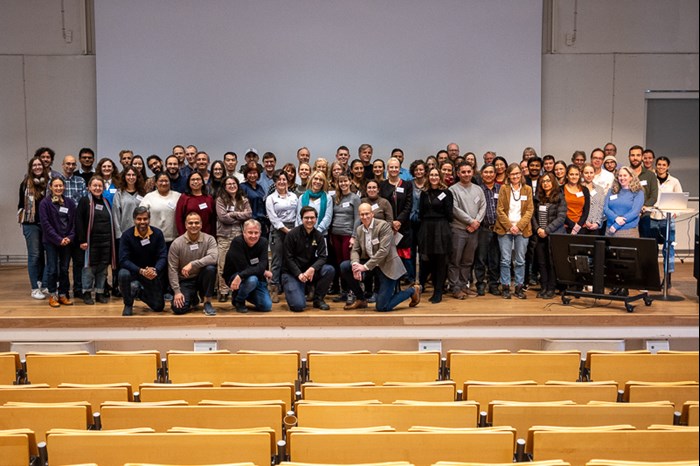 Around 80 people standing on a stage. Photo.