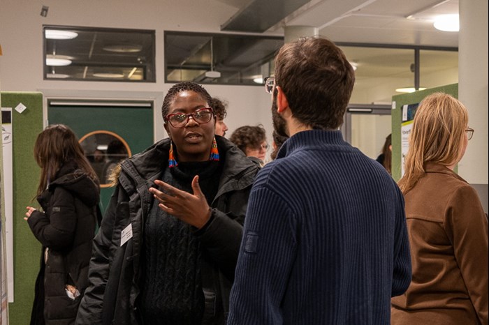 A woman talking in front of a poster. Photo.