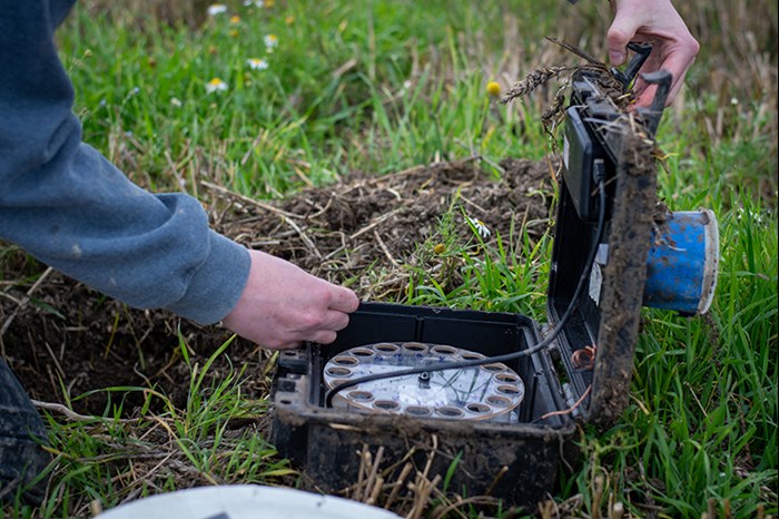 An opened plastic box in a field containing a round container with holes in it. Photo.