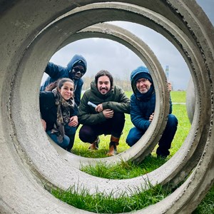 Four people peek through a large concrete pipe. Photo. 