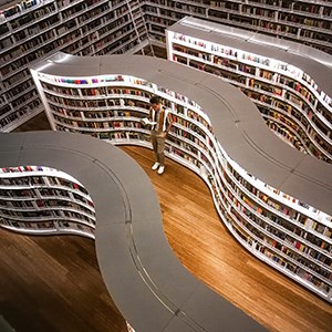 Bild ovanifrån på bokhyllor i ett bibliotek och en person som står och läser i en bok. Foto.