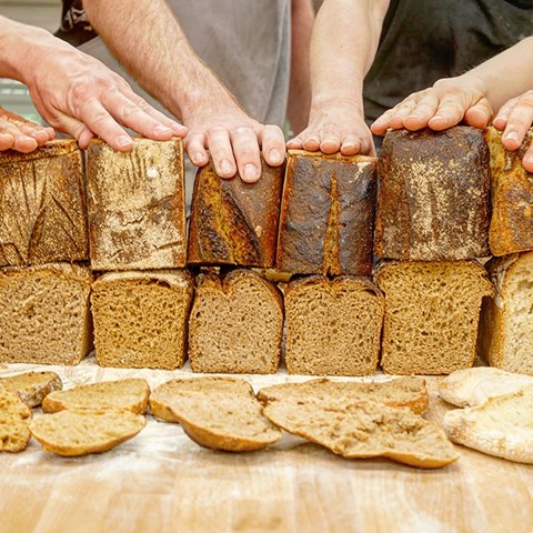 On a table many bread loafs, hands holding the breads. Photo.