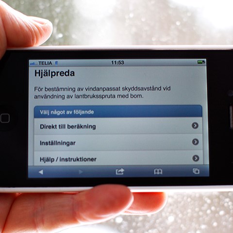 Mobiltelefon med en app med text om avstånd vid användning av lantbruksspruta med bom, foto.