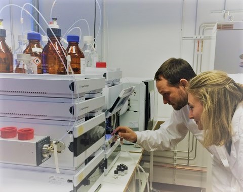 Two chemists examine an analysis instrument, photo.