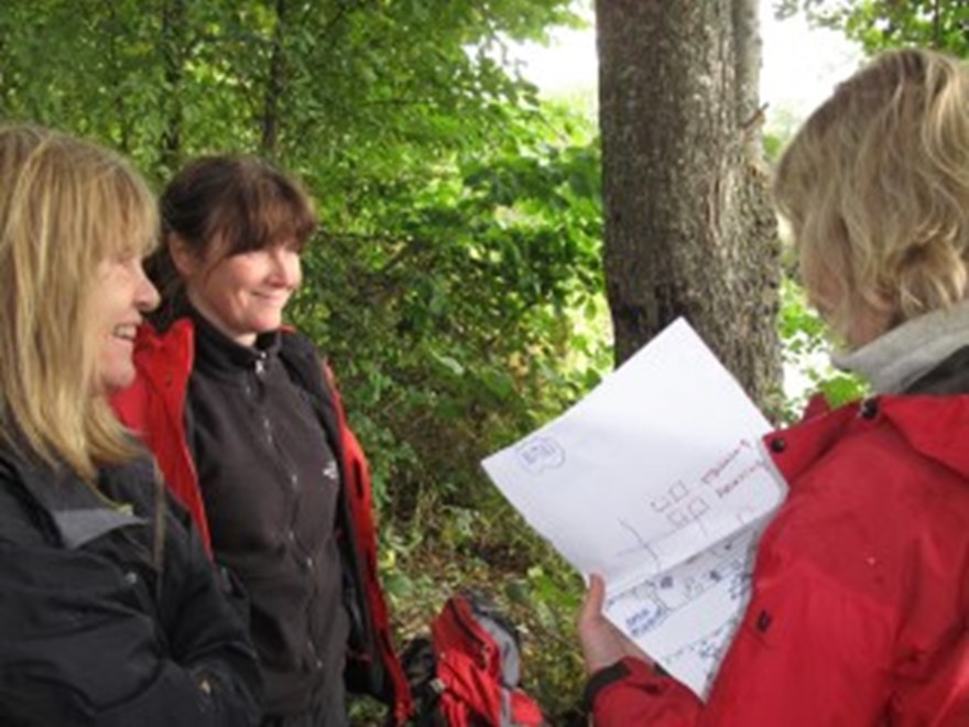 Tre personer utomhus. En håller i ett papper. Foto.