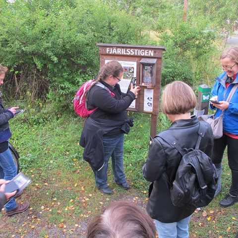 A group of people outdoors in front of an information board. Photo.