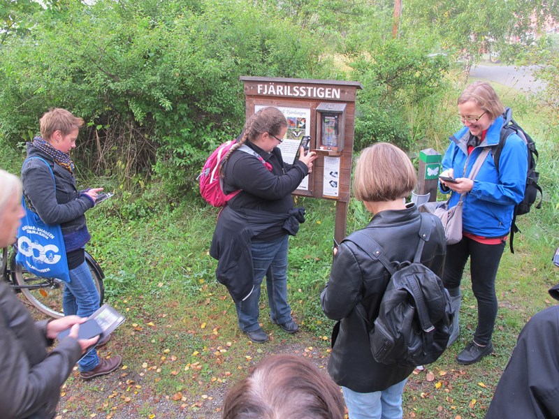 A group of people outdoors in front of an information board. Photo.