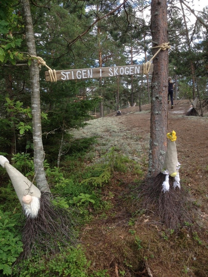 Skylt upphängd mellan två träd: ”Stigen i skogen”. Foto.