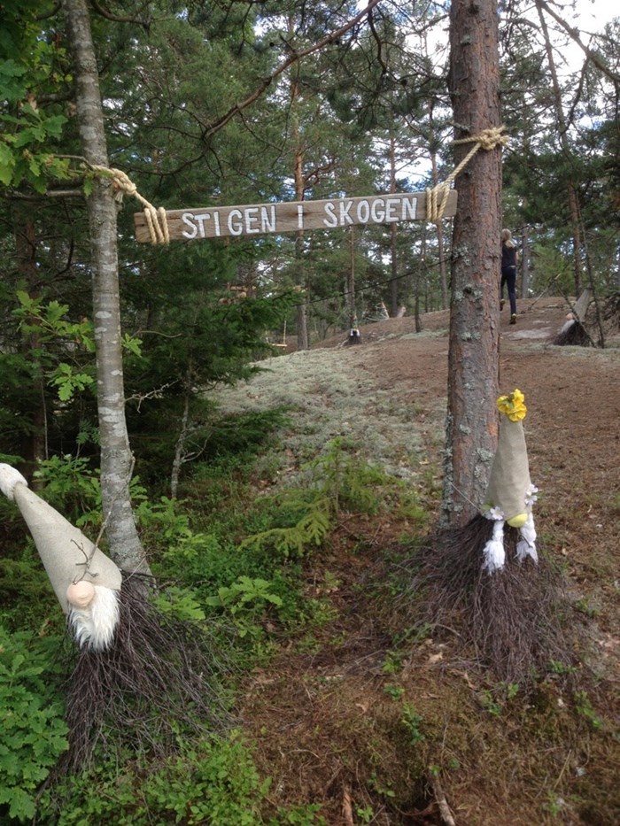 Skylt upphängd mellan två träd: ”Stigen i skogen”. Foto.