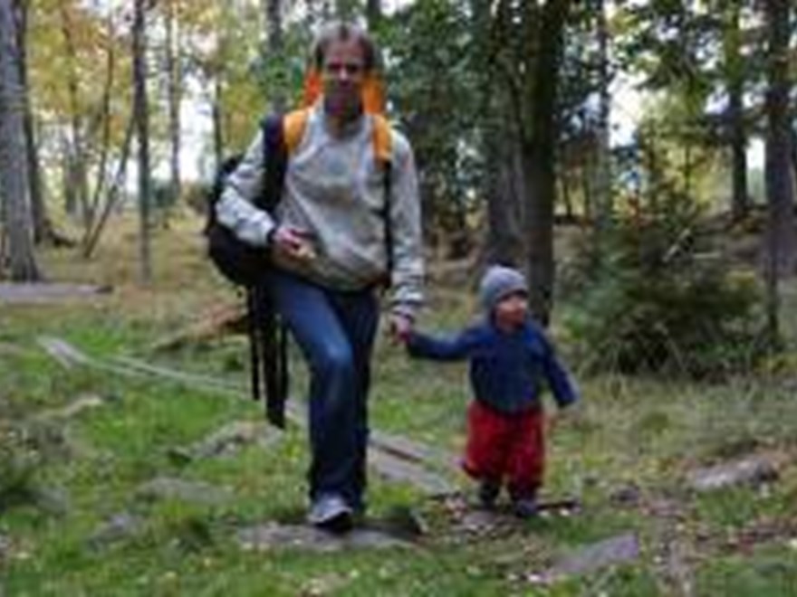 En vuxen och ett barn som promenerar i skogen. Foto.