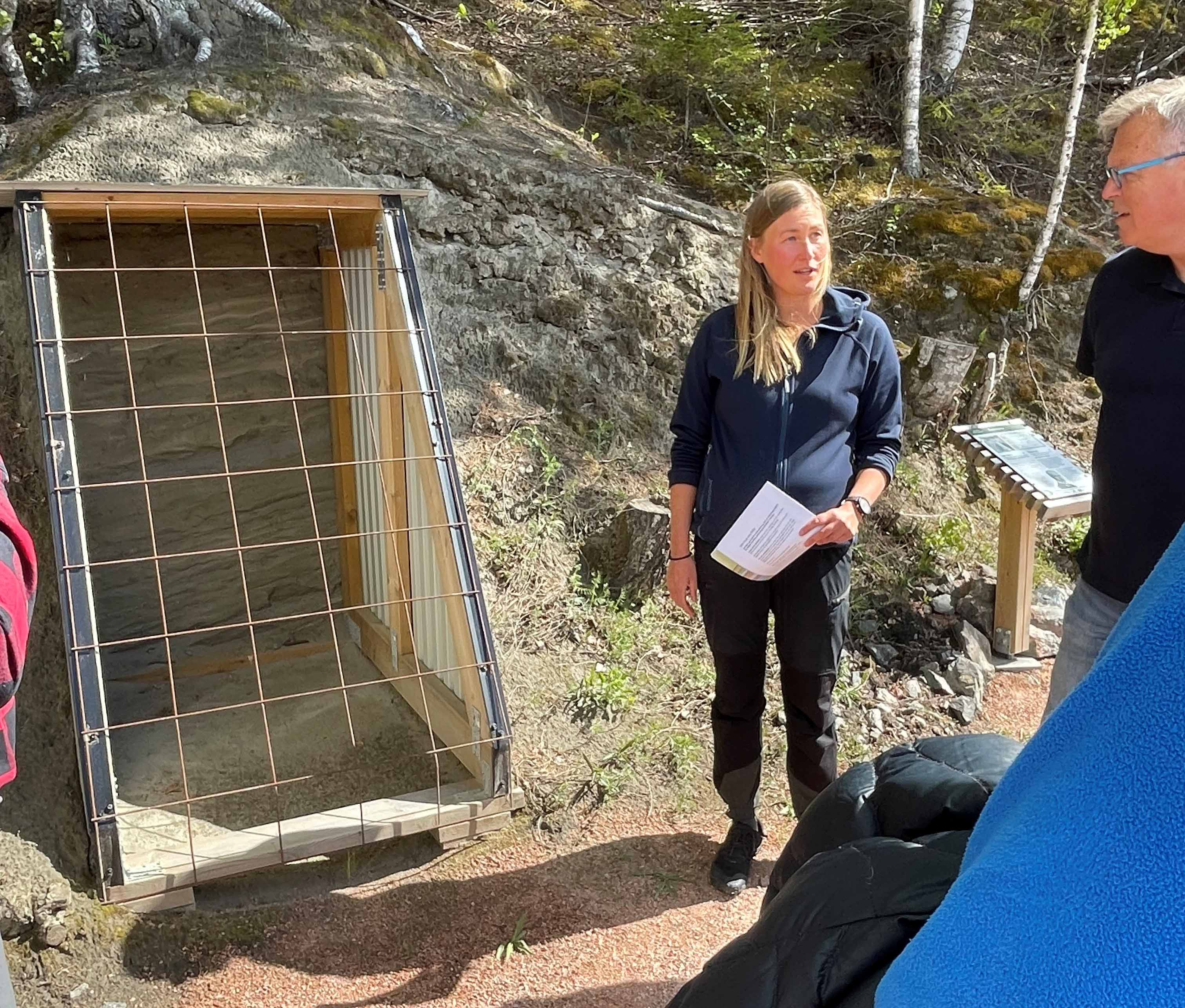 En guide står med sin grupp framför en utskärning av en ås. 