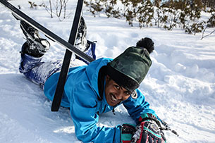 En man med skidor, som ligger i snön. Foto.