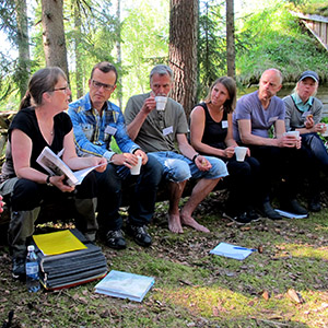 Sex personer sitter bredvid varandra i skogen. Foto.