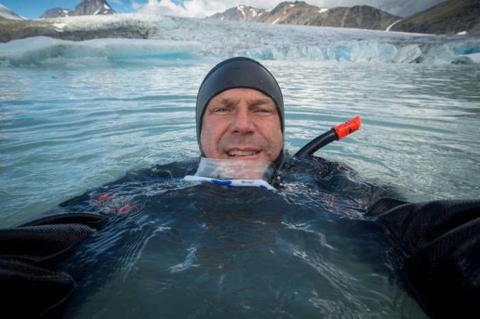 En man med dykarkläder i vatten. I bakgrunden is. Foto.