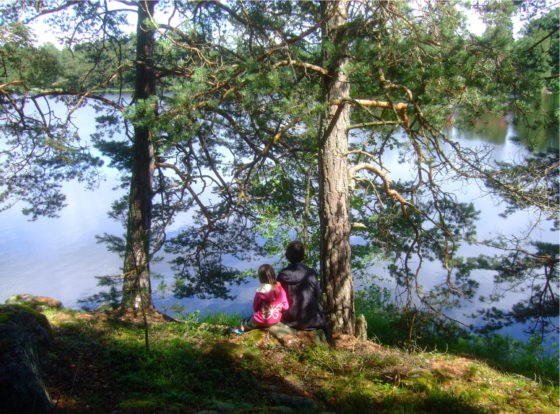 Barn sitter under en tall och blickar ut över en sjö.