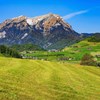 Kuperat jordbrukslandskap i Schweiz med små stugor utspridda, snöklädd alp bakom