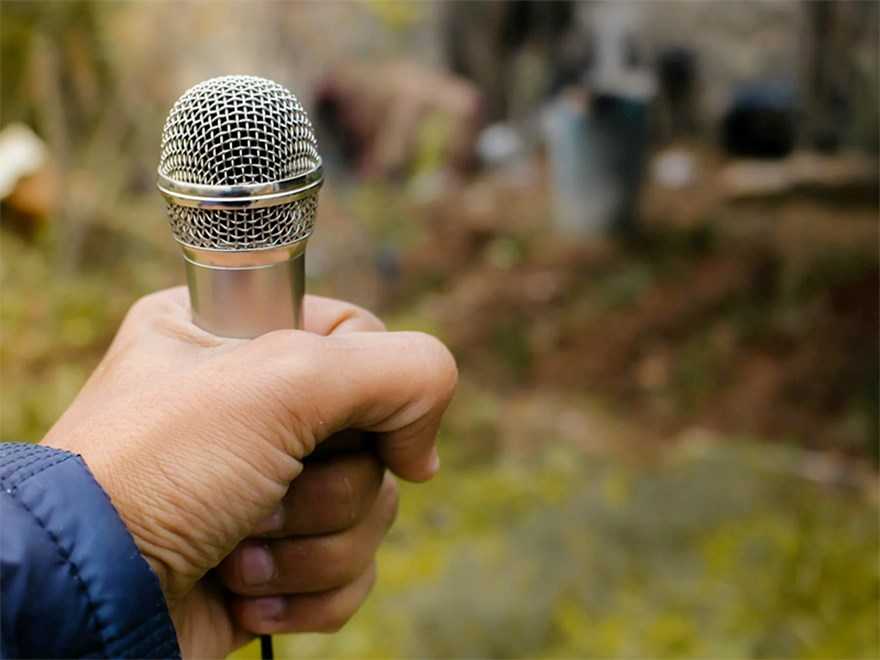 En hand håller i en mikrofon utomhus. Foto.