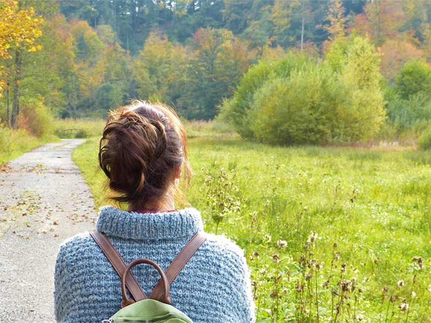 A woman from behind and a road, in the background there is a forest. Photo.
