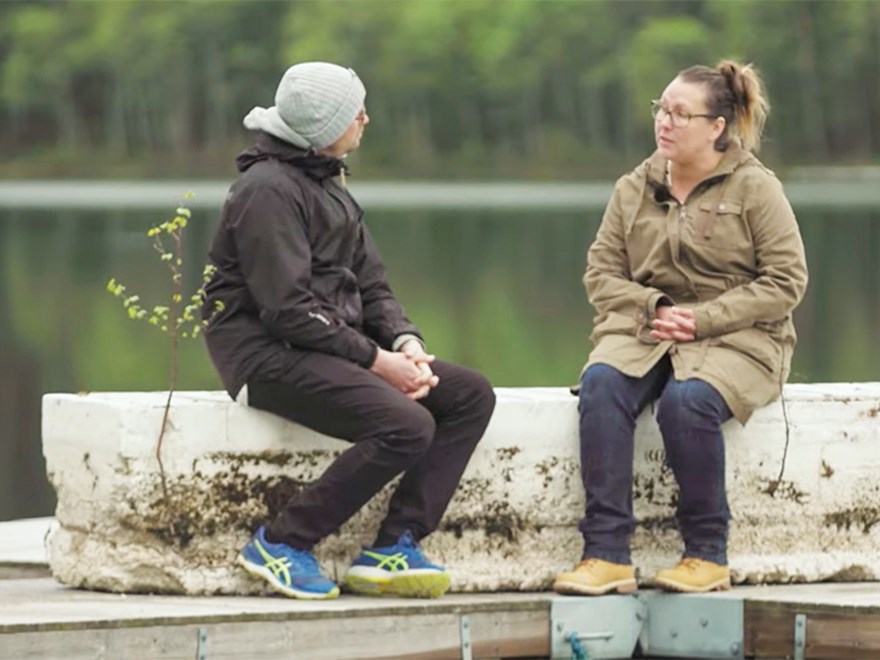 En man och en kvinna sitter vid en sjö. Foto.