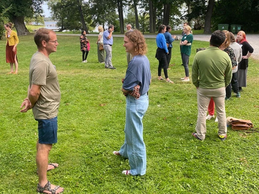 En grupp som står i cirkel utomhus på gräsmatta och pratar två och två.