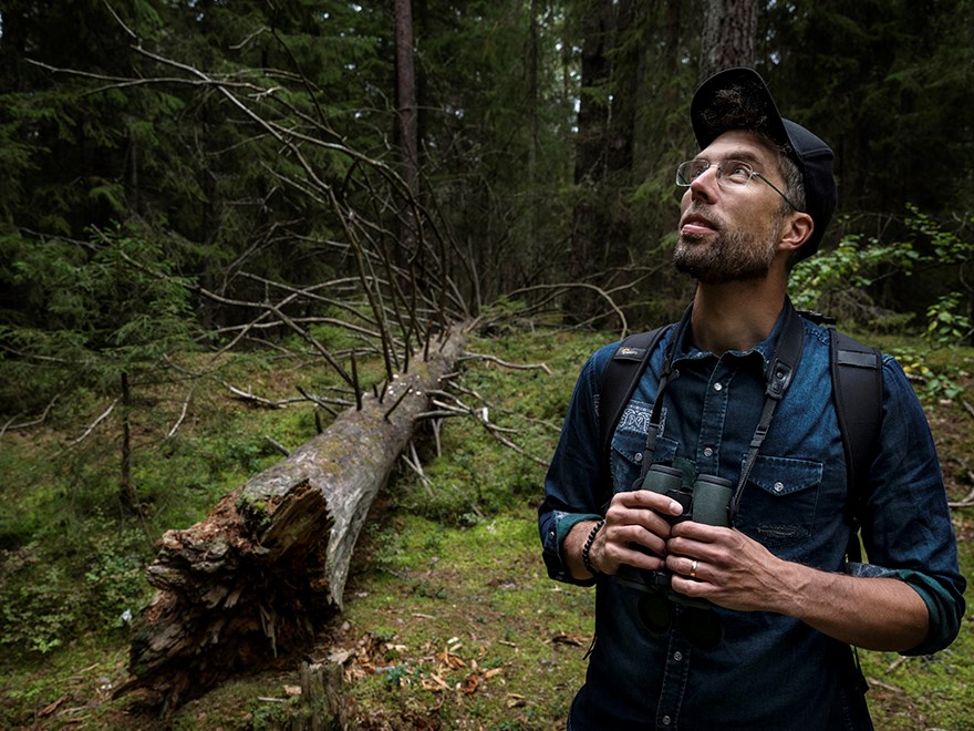 Marcus Hedblom with binoculars in forest.
