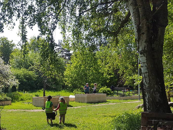 Two children carrying a water pitcher in a garden.