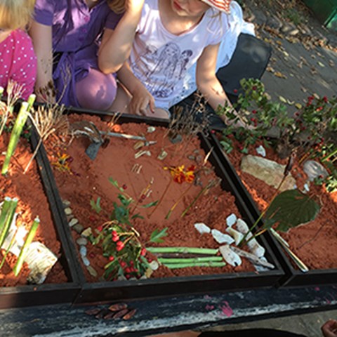 Children playing with models in sand.