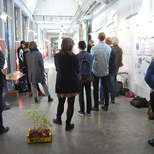 About 20 people discussing in front of a poster exhibition.
