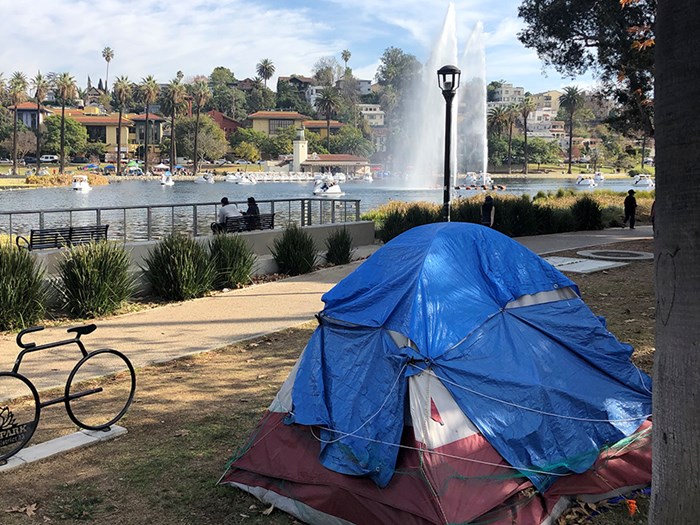 Tent next to a lake with a fountain and nice houses in the background.