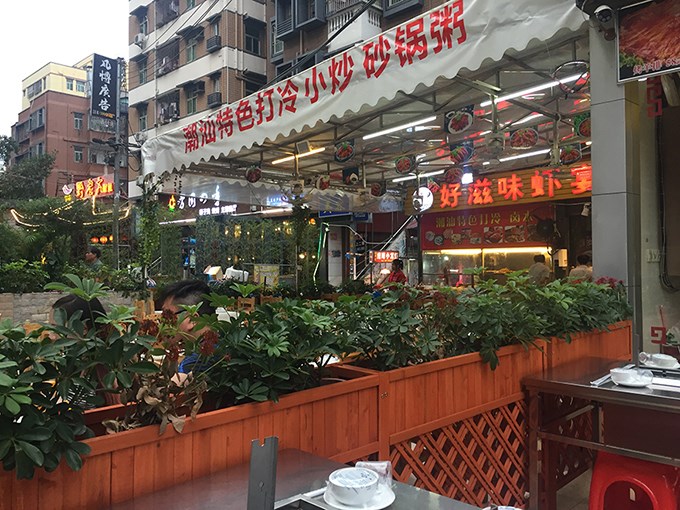 Restaurant in the urban village occupying the transitional zone between street and restaurant, one of dozens that line the street. The urban village housing rises behind the restaurant.