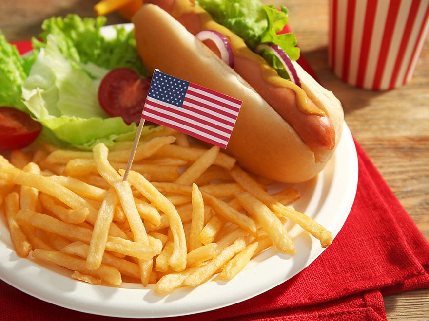 En tallrik pommes frites, en korv med bröd och en liten amerikansk flagga. Foto.