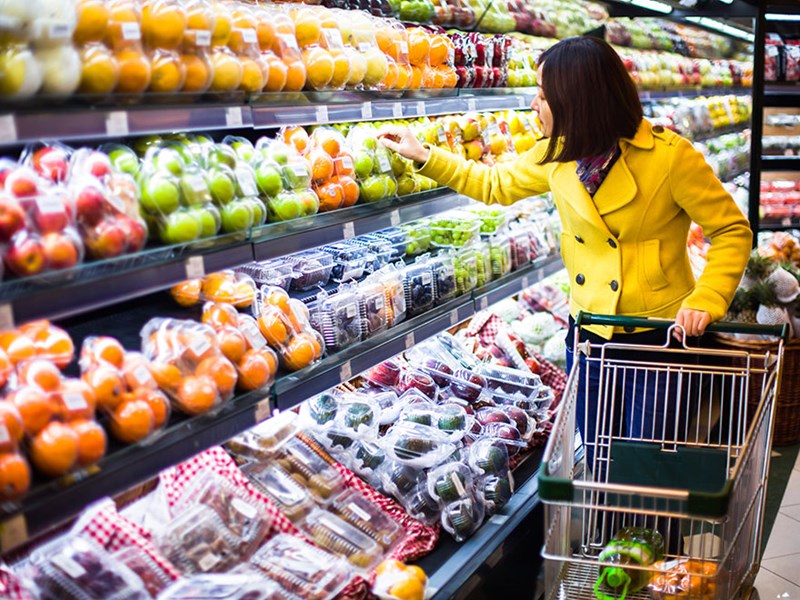 En kvinna med kundvagn väljer frukt i grönsaksdisken i en matvarubutik. Foto.
