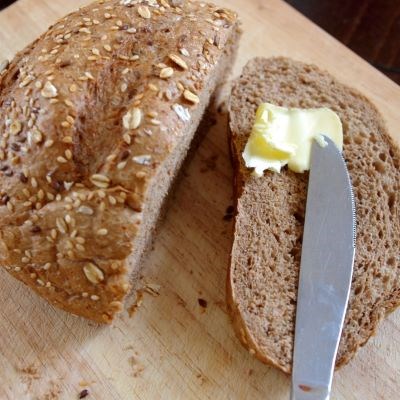 Smör eller margarin breds på en skiva mörkt bröd. Foto.