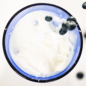 Blåbär faller ner i ett glas med mjölk. Foto.