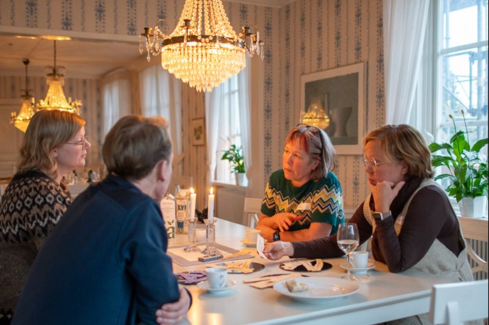 Four people sit at a table under a crystal chandelier. Photo.