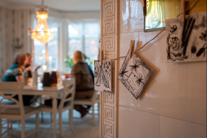 Drawings in the foreground, people at a table in the background. Photo.