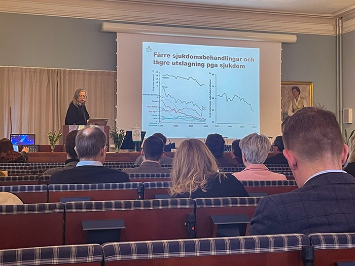 En kvinna vid en presentation framför publik. Foto.