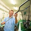 Forskaren Anders Kiessling håller upp en håv med fiskar från en experimentell fiskodling inomhus, foto.