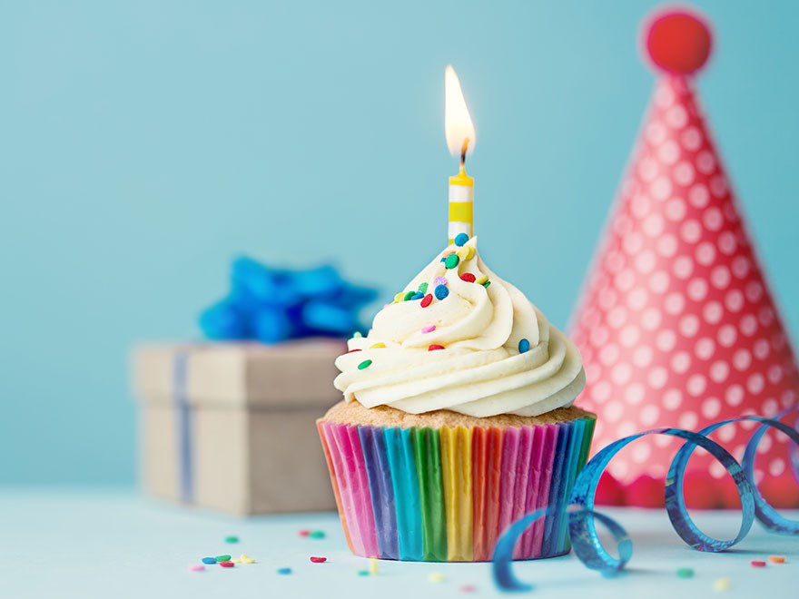 Färgglad muffin med ett tårtljus, partyhatt och serpentiner