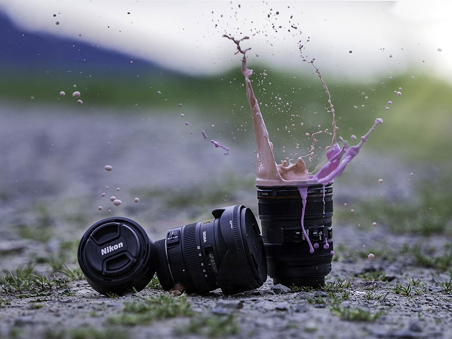 Parts for a system camera lies on the ground. Beige and purple liquid splash up from the lens. Photo.