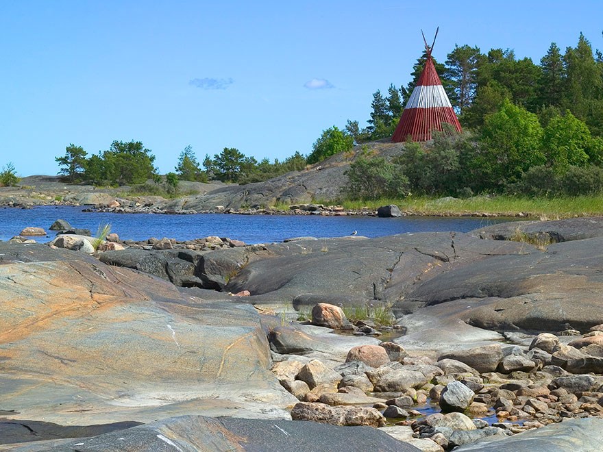 Ett rött och vitt sjömärke invid klippor vid havet. Foto.