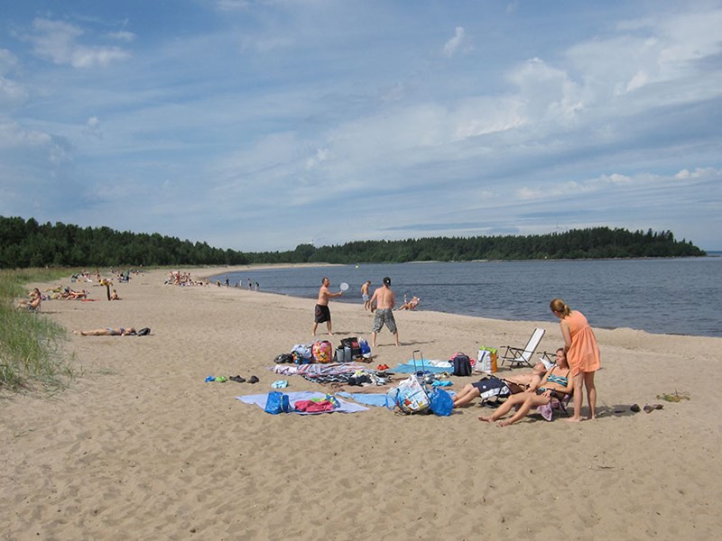 Människor leker och solar på en sandstrand. Foto.