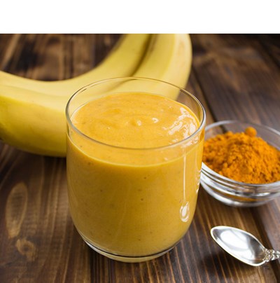 En orangegul smoothie, två bananer och en skål med kryddor. Foto.