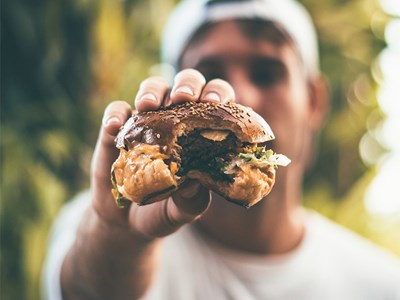 En man håller fram en hamburgare som han tagit en tugga av. Foto.