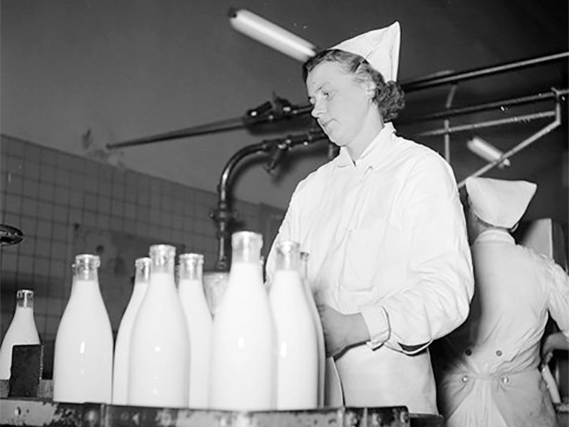 Svartvit bild av en kvinna med mjölkflaskor inomhus. Foto.