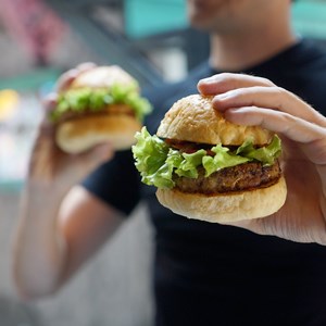 En person håller en hamburgare i varje hand. Foto.