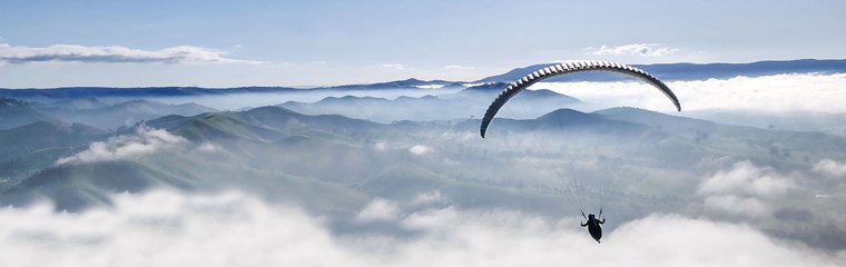 En skärmflygare högt över land och berg. Foto.