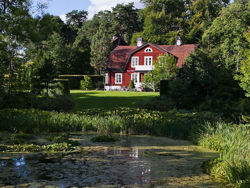 Rött trähus vid en damm. Foto.